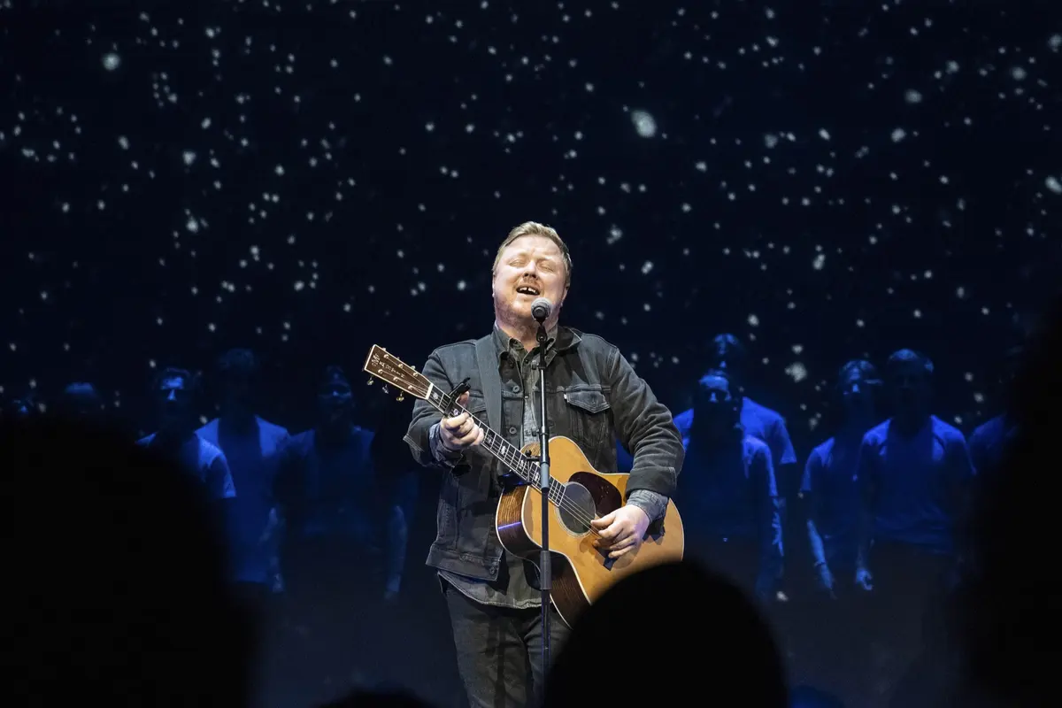 Solist synger med gitar foran stjerneteppet, sett over hodene på publikum
